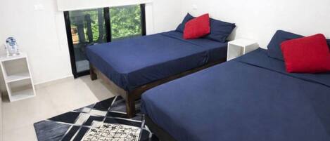 A modern bedroom with two beds, a geometric patterned rug, and a window with a view of greenery.