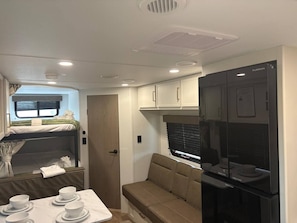 Interior compacto de um veículo recreativo, com cozinha compacta, área de refeições e beliche.