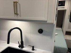 Una kitchenette compacta con un grifo moderno, un lavamanos pequeño y un sistema de ventilación integrado.