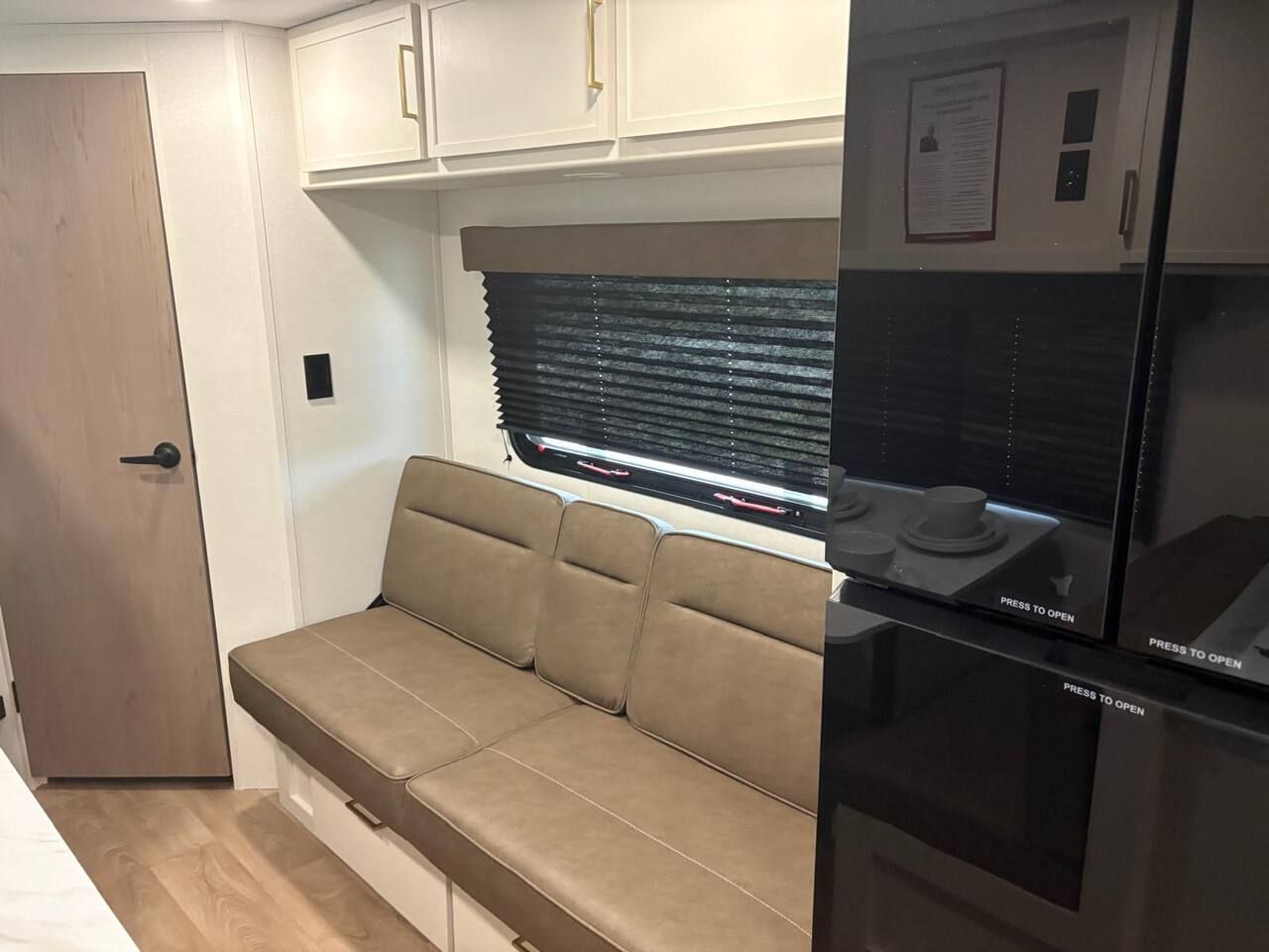 Una kitchenette compacta con refrigerador, una banca con espacio de almacenamiento y una ventana con persianas.