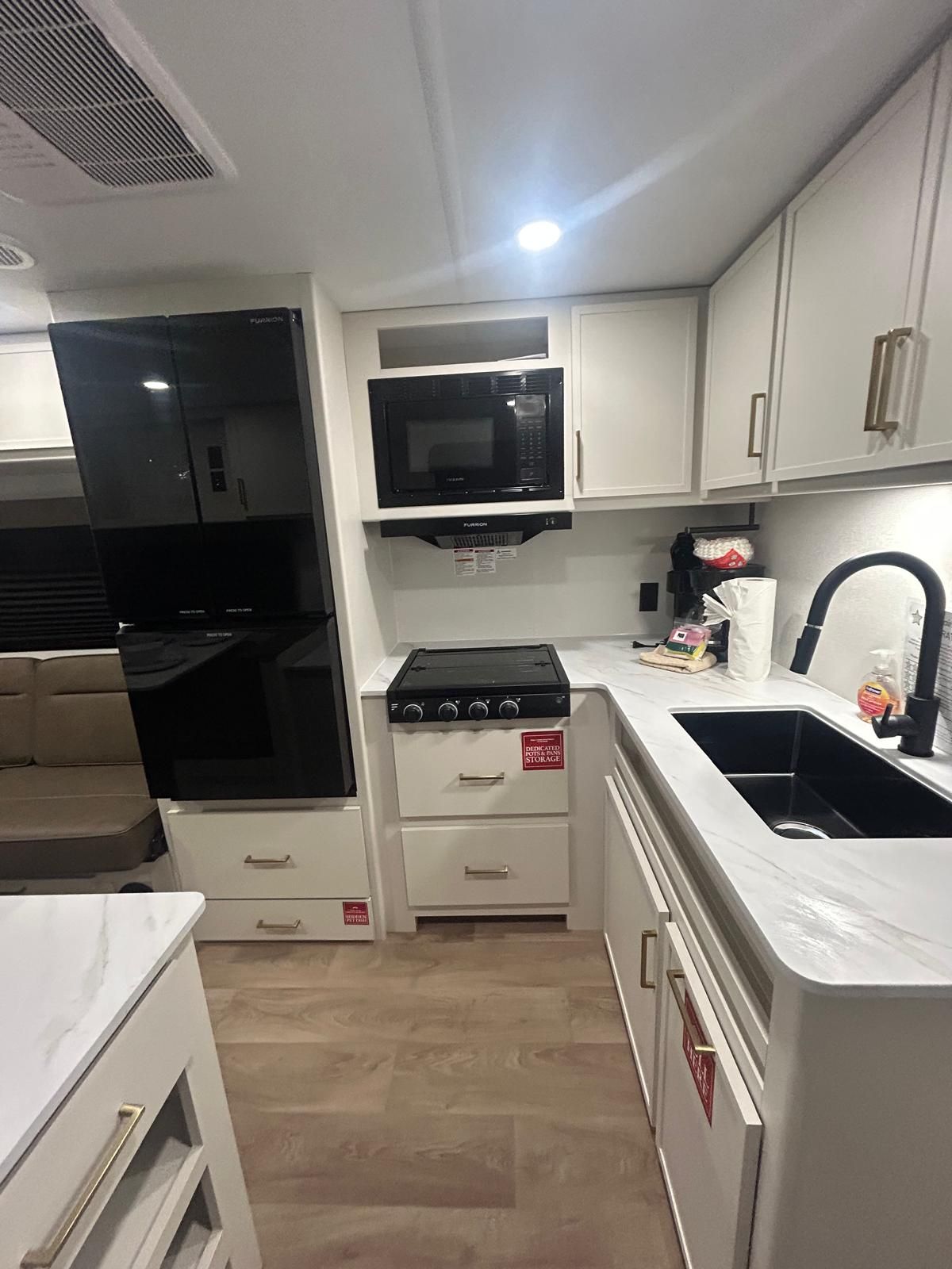 A compact kitchen with white cabinets, a black microwave, a stove, and a sink.