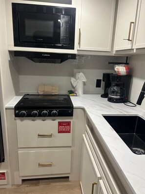 Una cocina compacta con microondas negro, estufa y espacio de almacenamiento para ollas y sartenes.