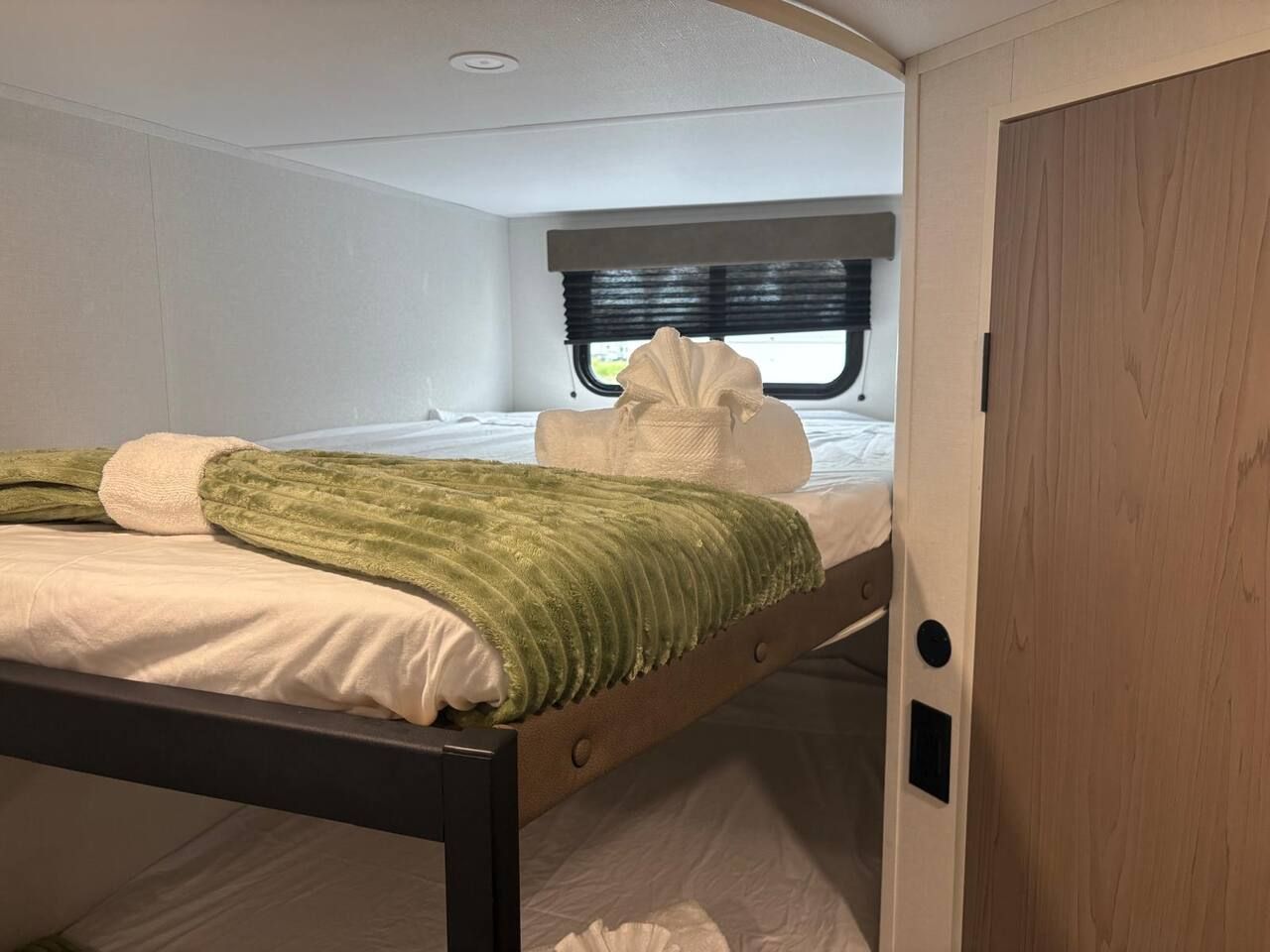 Un dormitorio compacto con literas, una ventana con persianas y una puerta con picaporte.