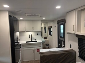 A compact kitchen with white cabinets, a sink, and a window with blinds. - Grand Design RV Getaway – #8, Rollover Bay & Ocean (Bolivar Peninsula)