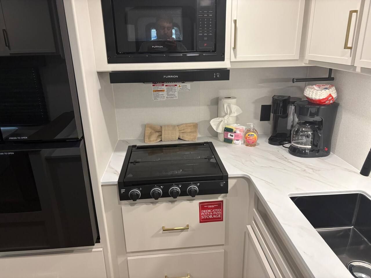 Cocina compacta equipada con microondas, estufa y almacenamiento específico para ollas y sartenes.