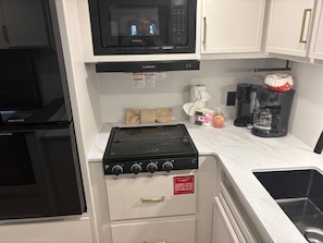 A compact kitchen with a microwave, stove, and dedicated storage for pots and pans. - Bayfront views | walk to Beach | Great Fishing #8, Rollover Bay Fishing Pier (Bolivar Peninsula)