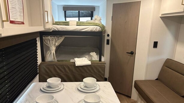 A compact RV interior with a dining table, a bunk bed, and a seating area.