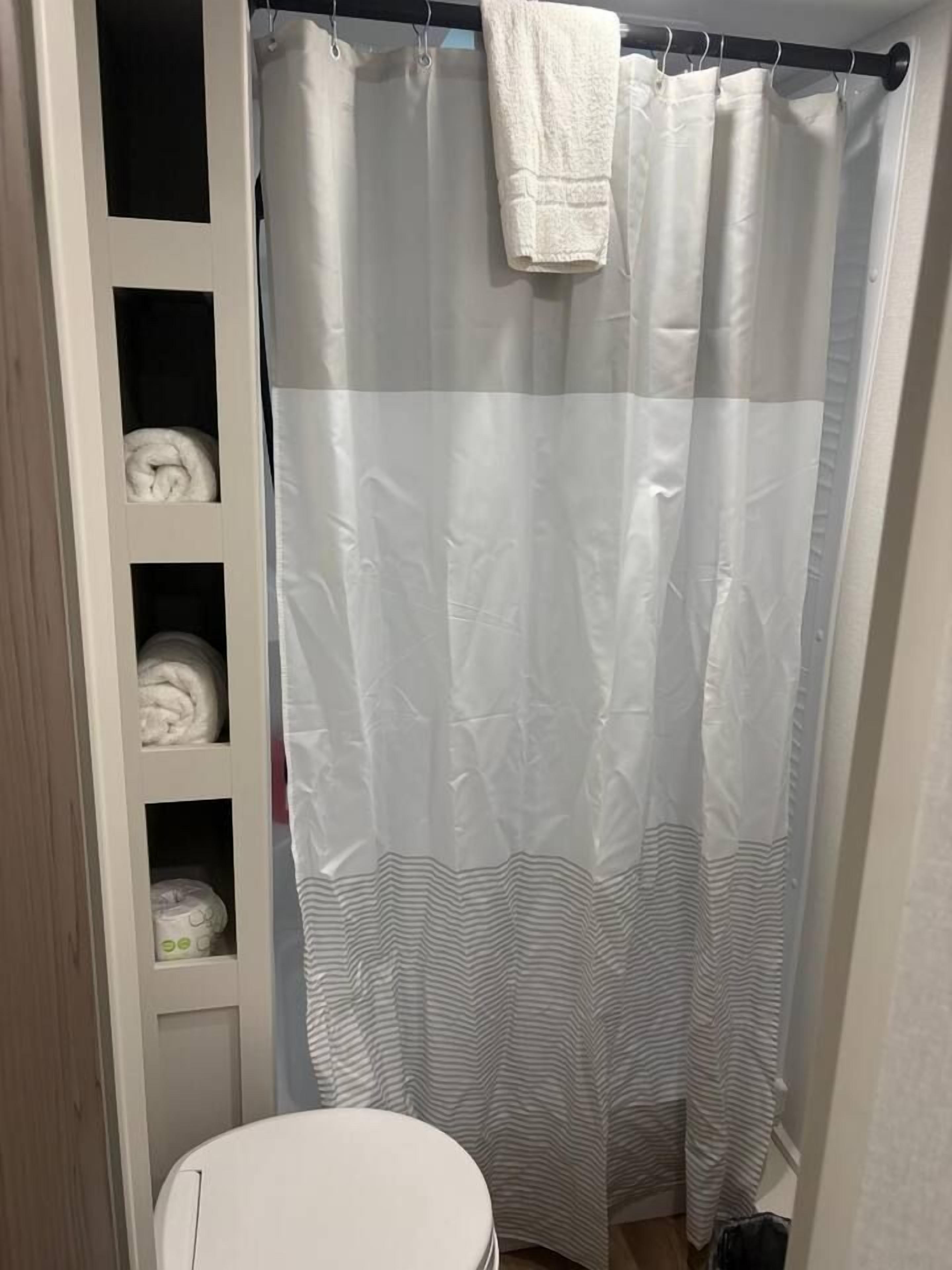 Un baño con cortina de ducha, inodoro y estantes con toallas.