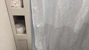 A white toilet with a closed lid, a striped shower curtain, and a shelf with a rolled towel and a trash bin. - Grand Design RV Getaway – #8, Rollover Bay & Ocean (Bolivar Peninsula)