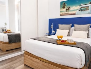 A hotel room with a bed, a tray of breakfast items, and a painting of a beach scene. - Charming Suite Living4Málaga (malaga)