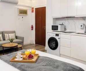 A compact living space with a sofa, a small table, a washing machine, a microwave, and a tray with breakfast items. - Charming Suite Living4Málaga (malaga)