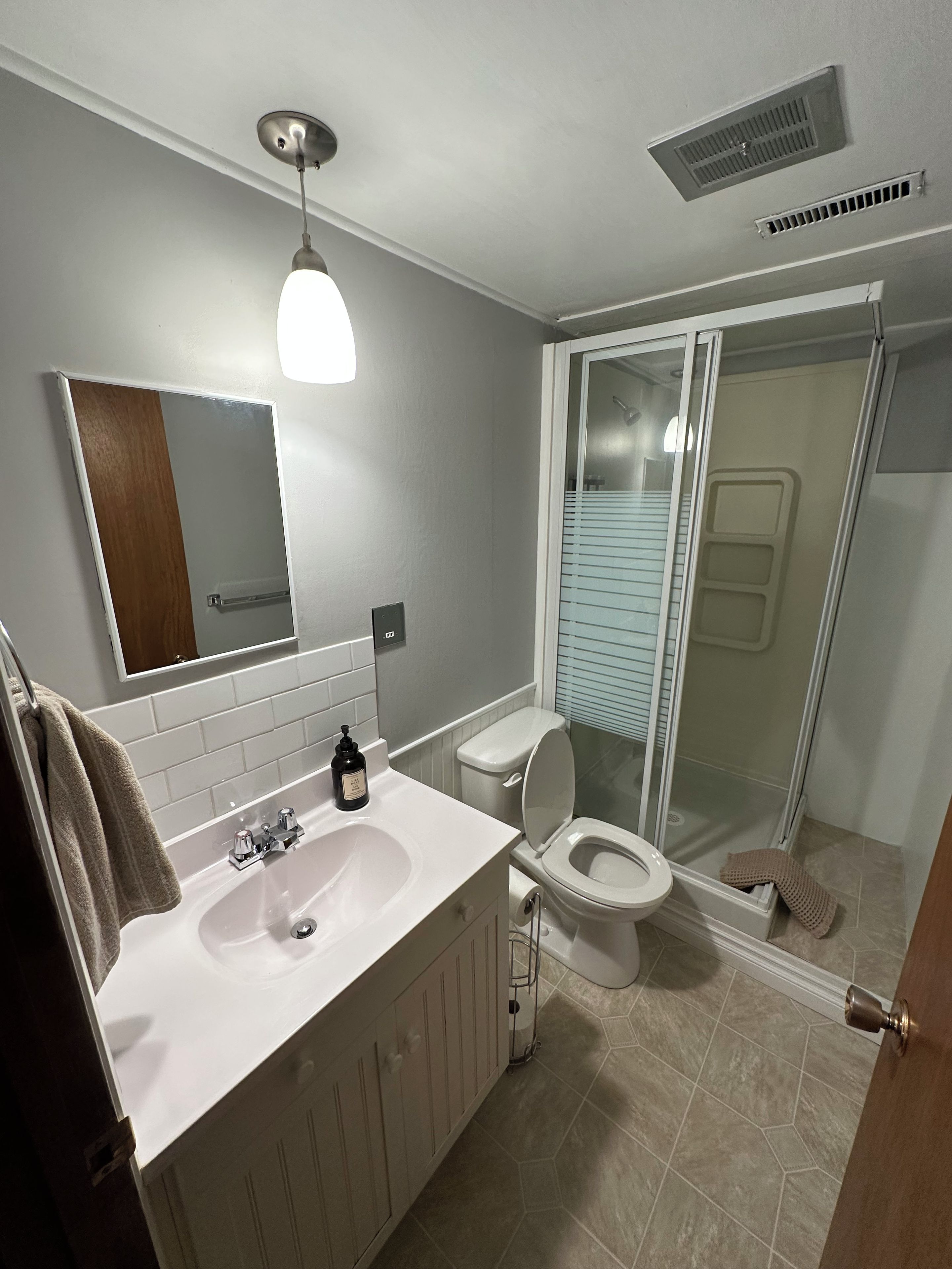 A bathroom with a white sink, mirror, and toilet. There is a shower area with a glass door.