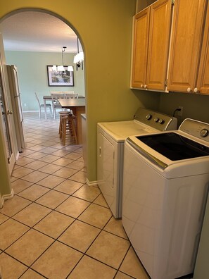 A laundry area with a washing machine and dryer, a dining table with chairs, and a kitchen with wooden cabinets.