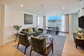 A modern living room with a sofa set, chairs, a coffee table, and a view of a cityscape through large windows. - Central Te Aro 2BR with Balcony & City Views (Wellington)