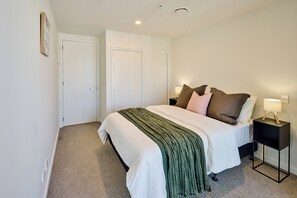 A bedroom with a bed, nightstands, a lamp, and a door. - Central Te Aro 2BR with Balcony & City Views (Wellington)