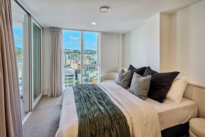 Ein Hotelzimmer mit einem grossen Bett, Blick auf eine Stadtkulisse durch raumhohe Fenster und einem Balkon.