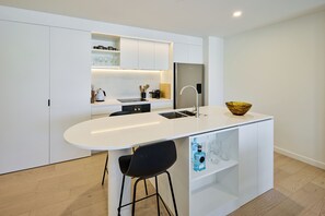 Eine moderne Küche mit einer zentralen Kochinsel, Barhocker, Backofen und Kühlschrank.