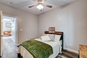 Een slaapkamer met een bed, een plafondventilator en een deur naar een andere kamer.