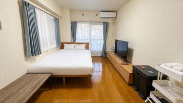 Una habitación de hotel con una cama, televisión, escritorio y un carrito pequeño con un cesto.