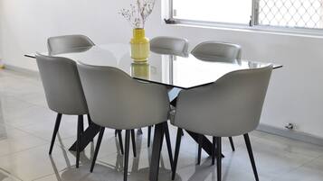 A modern dining area with a glass table surrounded by four grey chairs with black legs.