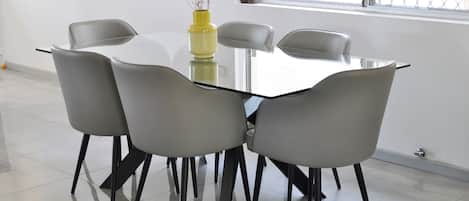 A modern dining area with a glass table surrounded by four grey chairs with black legs.