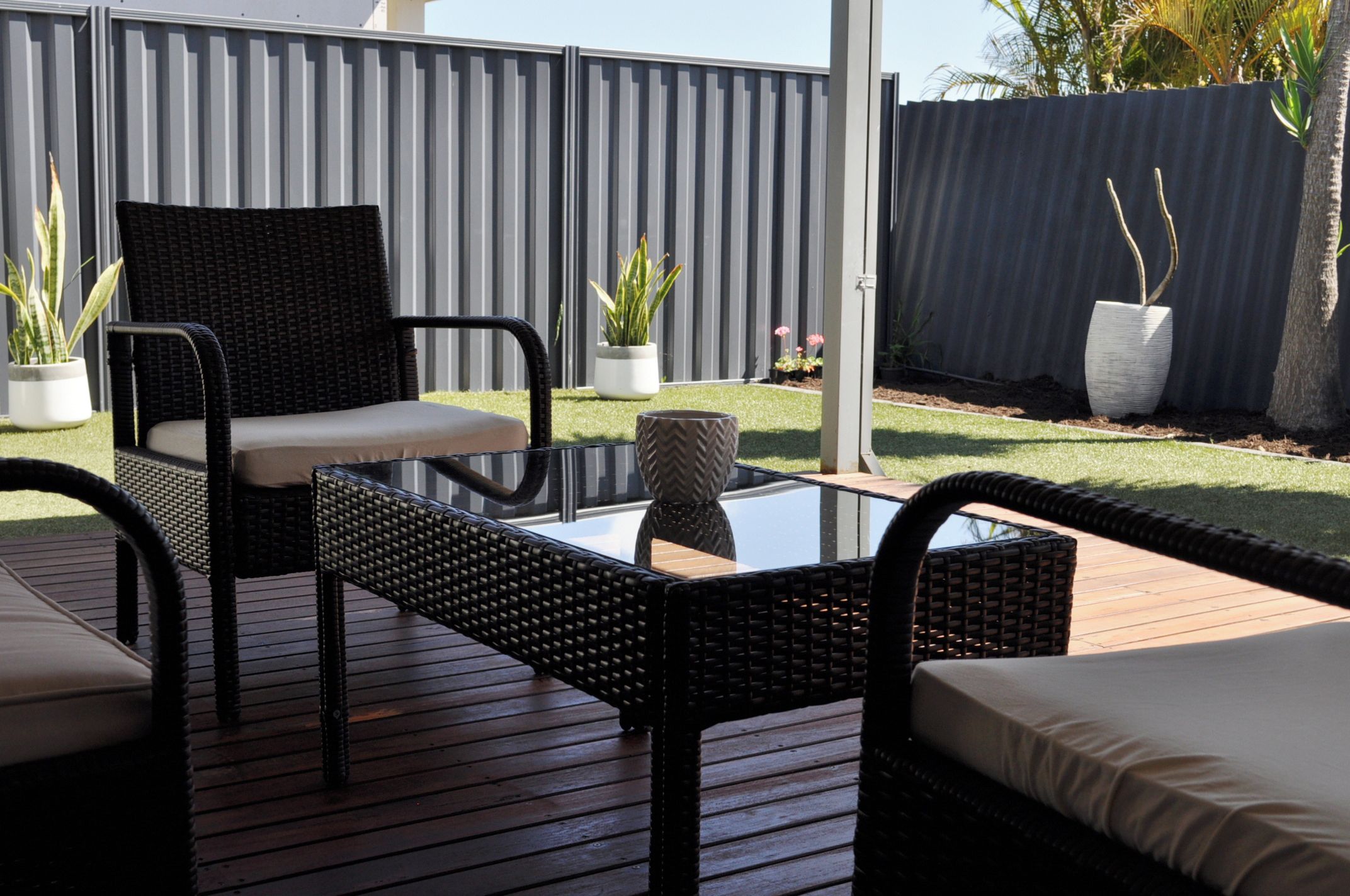 An outdoor patio area with wicker furniture, a glass table, and potted plants.