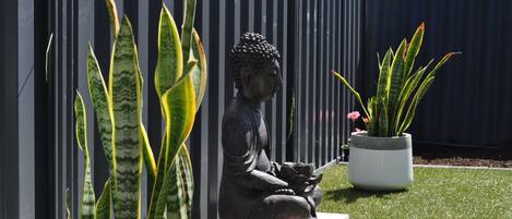 A garden with a Buddha statue, two potted plants, and a fence.