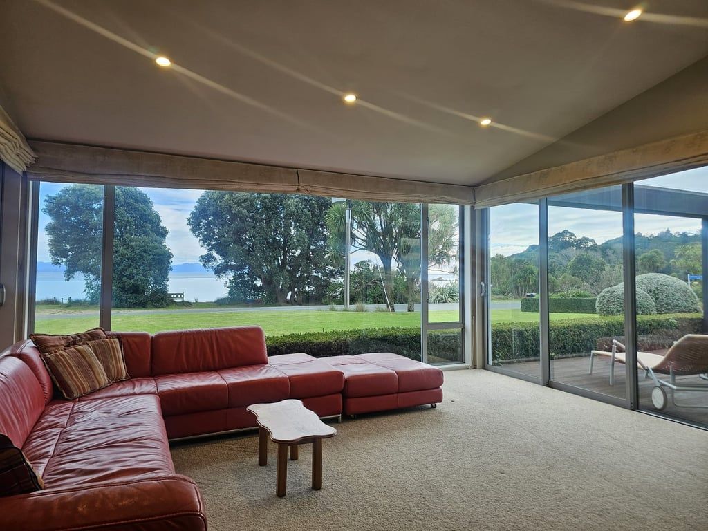 A modern living room with a red leather sofa, a small table, and large windows offering a view of a green landscape and water.