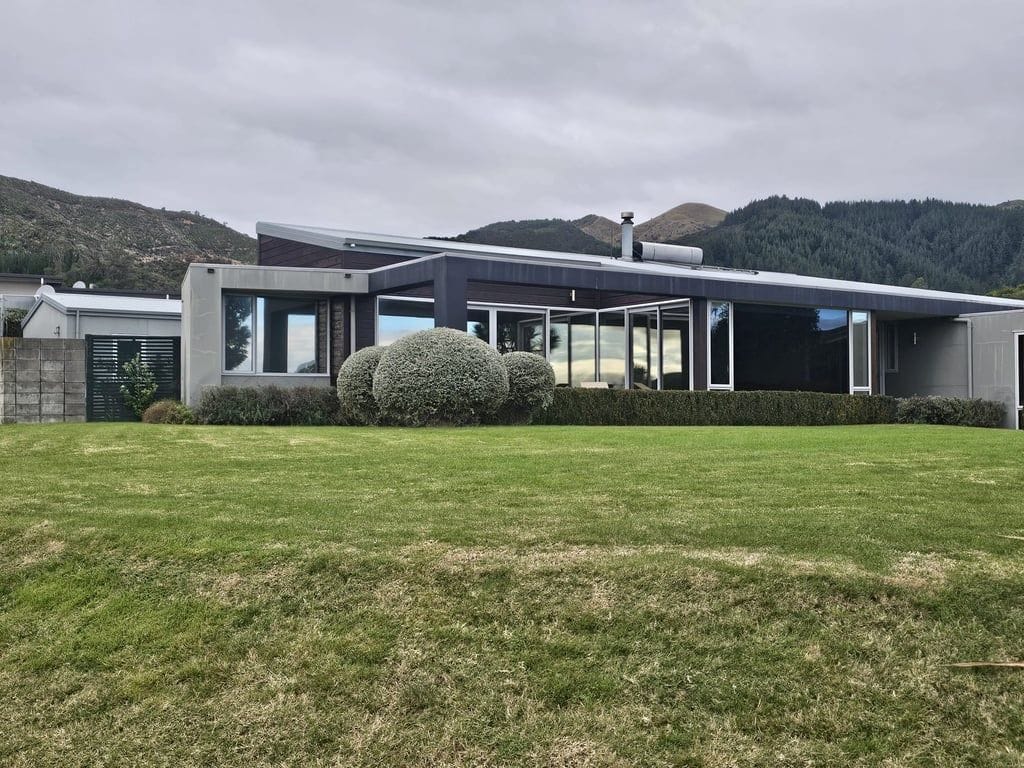 Une maison moderne dotée d’une grande façade vitrée, d’une pelouse bien entretenue et surplombant un paysage montagneux.
