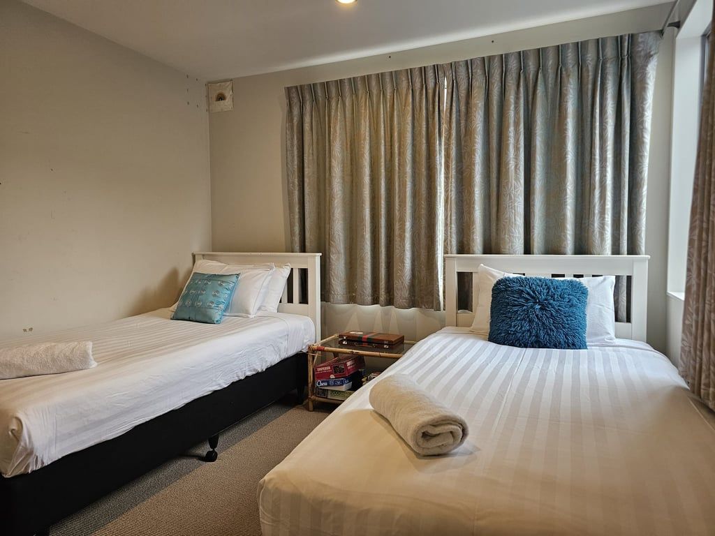 Ein Hotelzimmer mit zwei Betten, einem kleinen Tisch und einem Fenster mit Vorhängen.