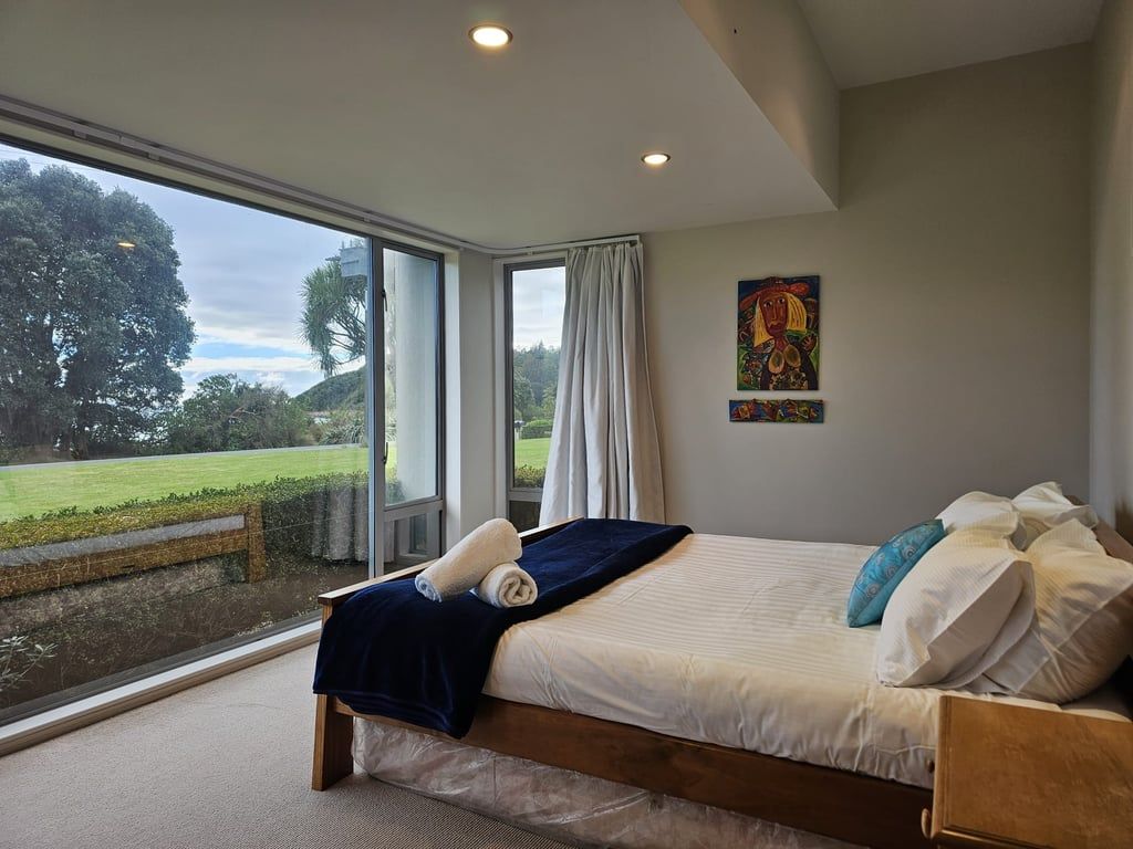 A bedroom with a large window, a bed, and a painting on the wall.
