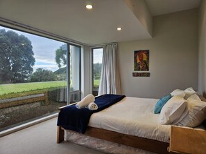 A bedroom with a large window, a bed, and a painting on the wall.