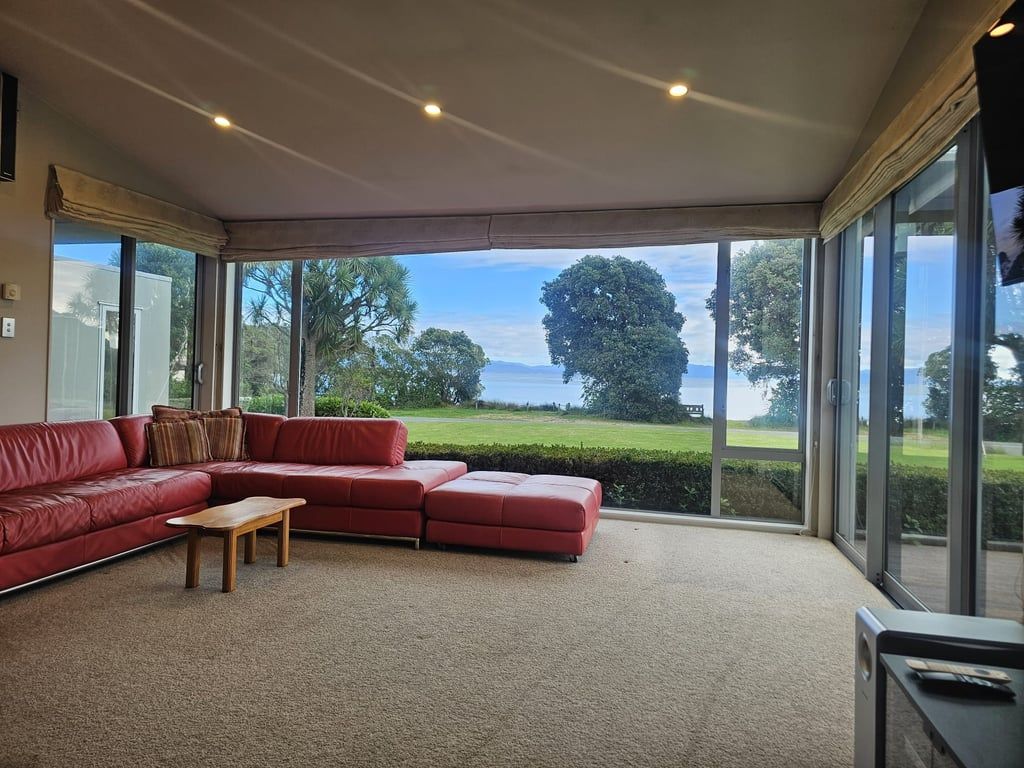 A spacious living room with a red sectional sofa, a wooden coffee table, and large windows offering a view of a green landscape and a body of water.