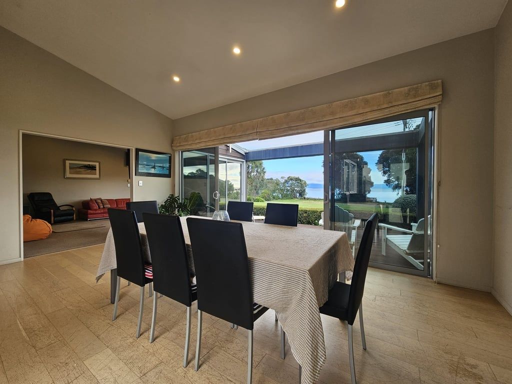 A dining area with a table and chairs, a sofa, and a view through glass doors.