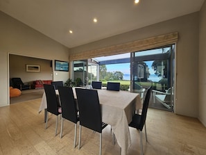 A dining area with a table and chairs, a sofa, and a view through glass doors.