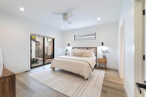 Un dormitori amb un llit, taules de nit, un ventilador de sostre i una porta corredissa de vidre que dona a una zona exterior.
