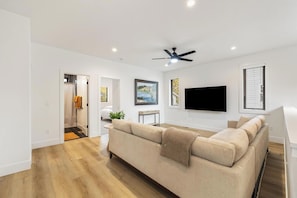 Ein modernes Wohnzimmer mit einem beigefarbenen Sofa, einem an der Wand montierten Flachbildfernseher und einem Deckenventilator.