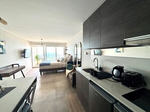 A modern hotel room with a kitchenette, a bed with a view, and a dining area. - Cozy 1 bedroom apartment with a sea view + heated pool + parking in Reñaca. (Viña del Mar)