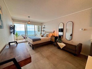 Ein Schlafzimmer mit Bett, Nachttischen, einem Schminktisch, einem Sofa, einem Schreibtisch und Blick auf das Meer.