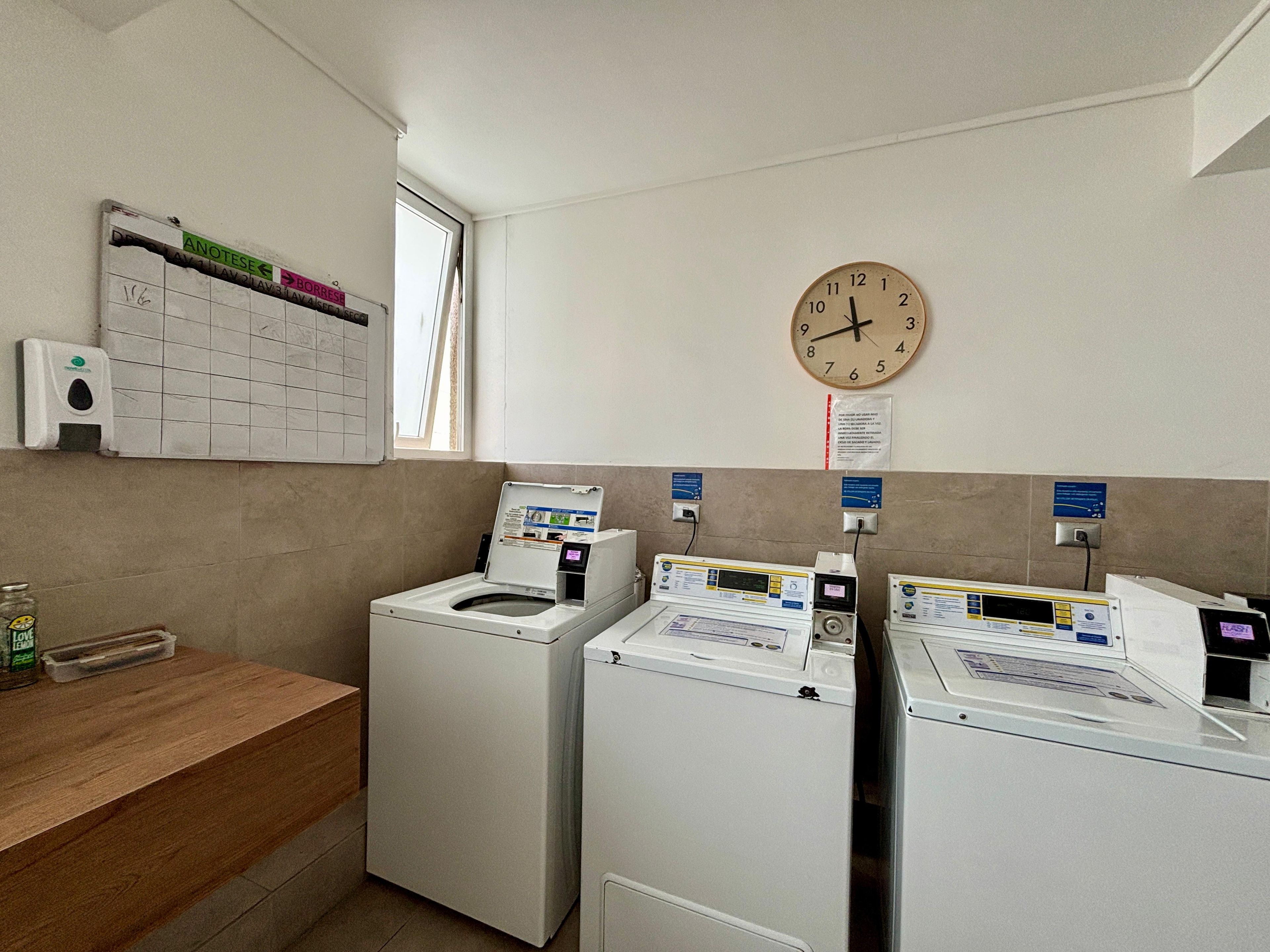 Une buanderie équipée de deux machines à laver à chargement frontal, d’un plan de travail en bois, d’une horloge murale et d’une fenêtre.