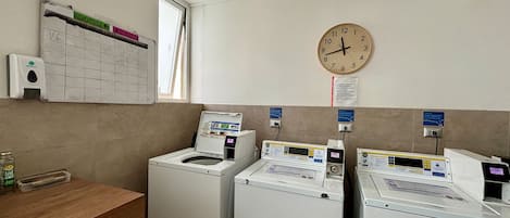 Une buanderie équipée de deux machines à laver à chargement frontal, d’un plan de travail en bois, d’une horloge murale et d’une fenêtre.