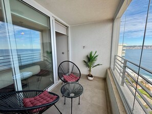 Ein Balkon mit zwei schwarzen Stühlen und einem Topfpflanzen, der Blick auf die Küste freigibt.