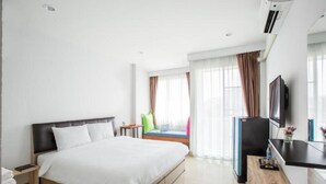 A hotel room with a bed, a desk, a television, and a window with curtains. - Baan I Inspire (Mueang Phrae District)