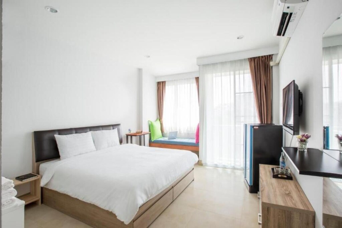 A hotel room with a bed, a desk, a television, and a window with curtains.
