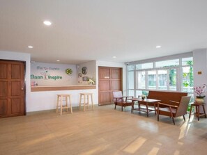 A spacious room with a wooden floor, a reception desk, a seating area with chairs and a table, and large windows. - Baan I Inspire (Mueang Phrae District)
