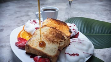 En tallerken med ristet brød, jordbær og flødeskum, med en kop kaffe og et glas gul drik i baggrunden.