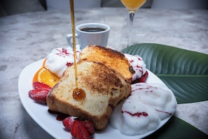 Um prato com torradas, morangos e chantilly, acompanhado de uma xícara de café e um copo de uma bebida amarela ao fundo.