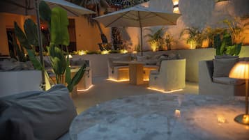 An outdoor seating area with a round table, cushioned chairs, and umbrellas providing shade.