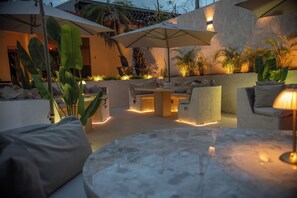 Un espace extérieur aménagé avec une table ronde, des chaises rembourrées et des parasols pour créer de l’ombre.