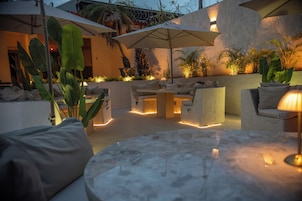 An outdoor seating area with a round table, cushioned chairs, and umbrellas providing shade.